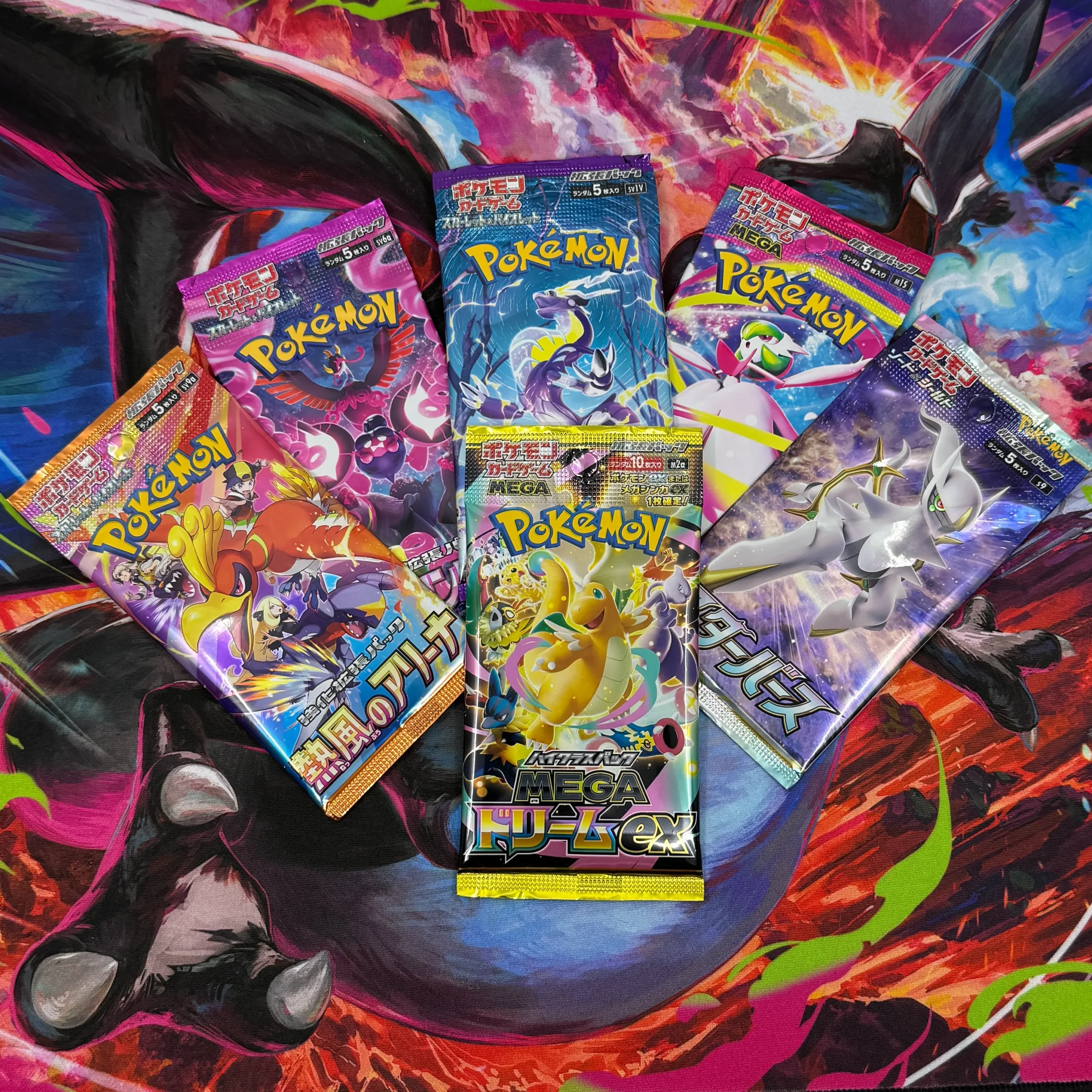 Six Japanese Pokémon TCG booster packs displayed on a colourful Charizard playmat for a pack opening video Six Japanese Pokémon TCG booster packs displayed on a colourful Charizard playmat for a pack opening video